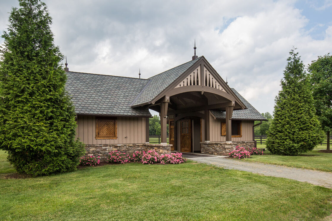 custom equine facility entrance building sitting amidst two large bushes with small flower beds sitting in front all sitting beneath a cloudy sky