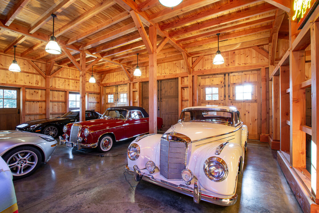 three visible high end cars with the front of a fourth partially visible to the left all sitting beneath illuminated light fixtures inside a custom garage