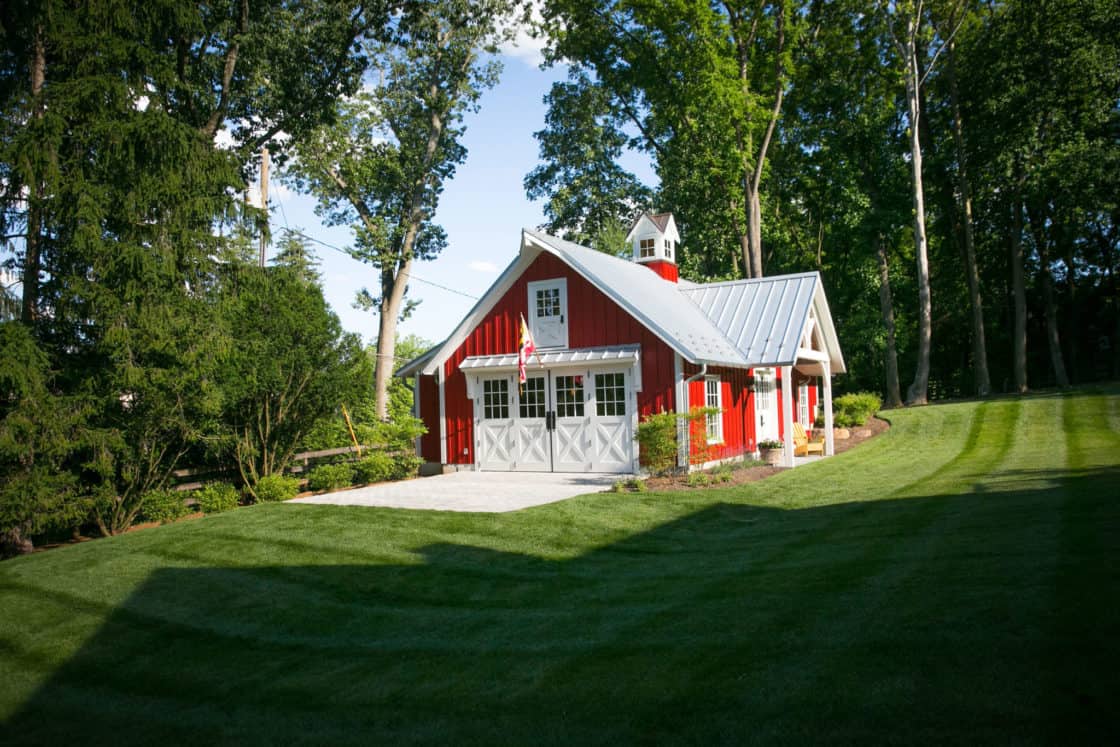 red custom garage with white door sitting amidst green grass, trees, and blue sky