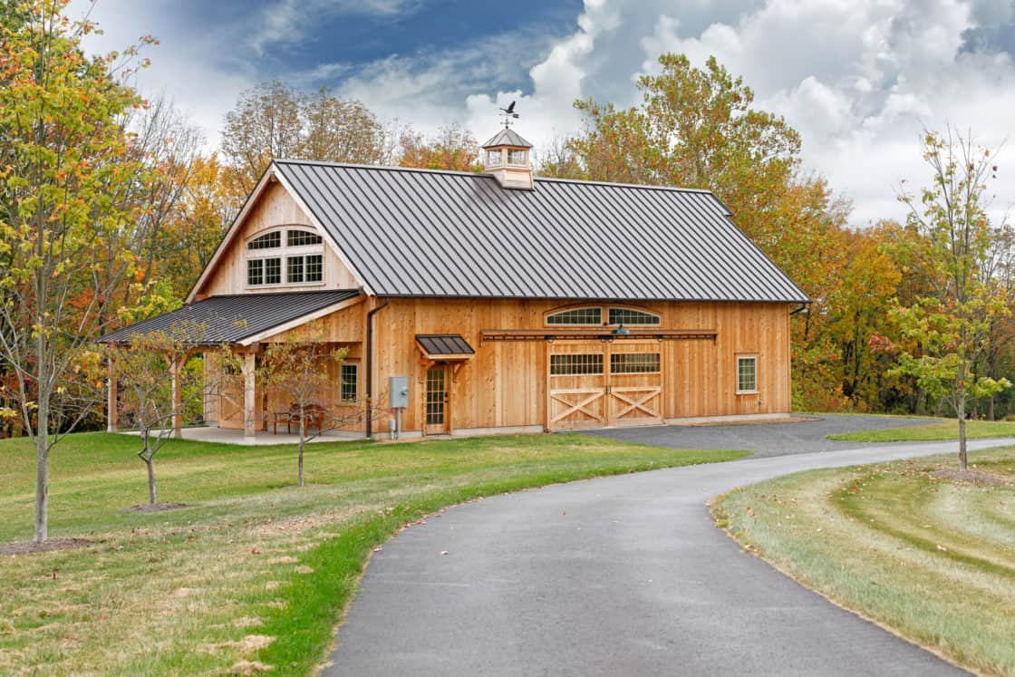 custom garage with metal roof sitting behind driveway and in front of wooded area