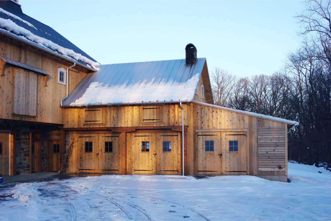 close up of bank barn stable doors sitting beneath metal roof that is half covered in snow