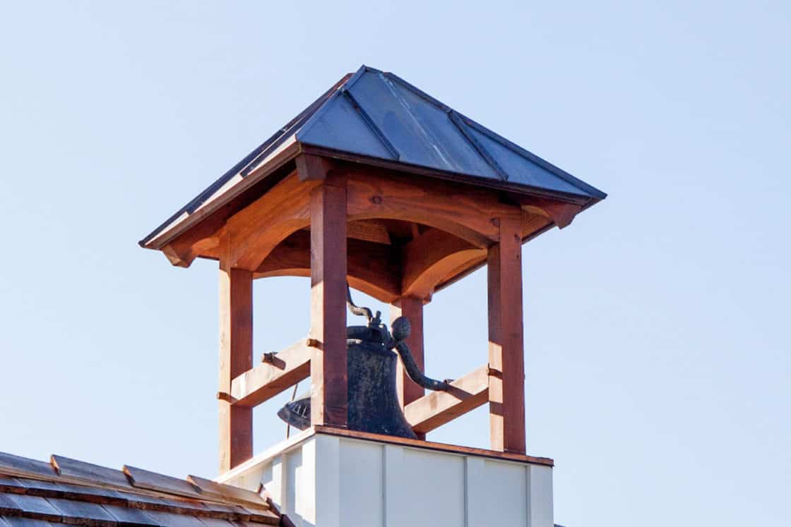 bell sitting on stop of shingled roof sitting beneath blue sky
