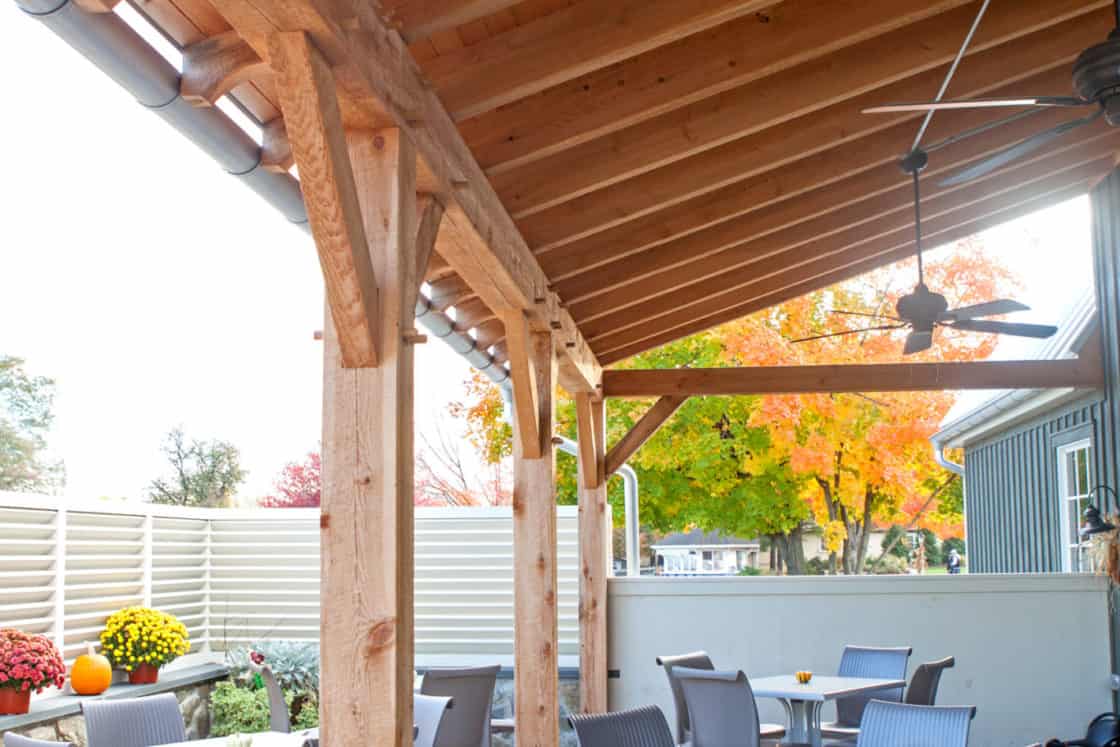 outdoor dining area with square tables and chairs partially beneath wooden overhang
