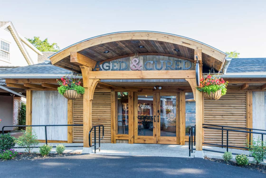aged & cured entryway with two symmetrical wooden and glass doors sitting in the center of building beneath shingle roof