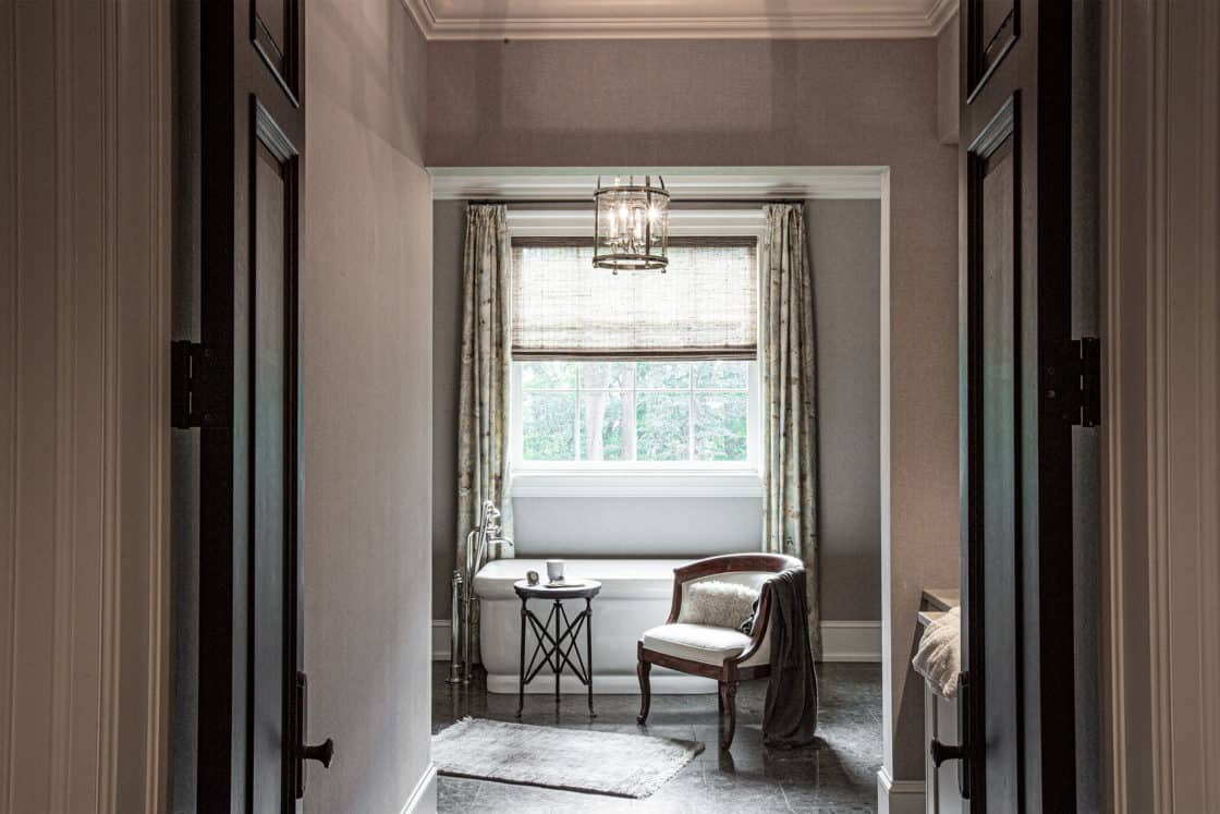 A cozy reading nook with a chair, small round table, and rug is set by a window with blinds and curtains. Neutral tones and a hanging light fixture evoke the serene comfort of a luxury home’s calm atmosphere.
