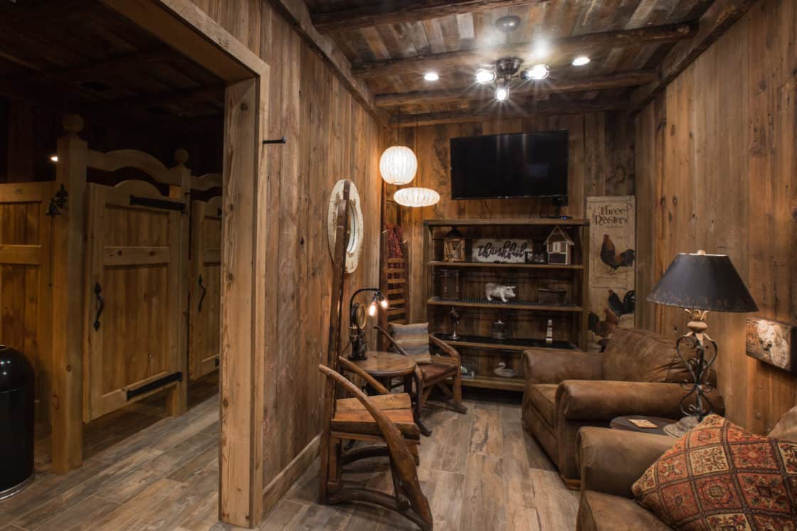 A cozy rustic room with wooden walls and floors, brown leather chairs, a bookshelf, and western-style decor evokes the charm of a party barn. Warm lighting and inviting touches add to this luxury home's welcoming atmosphere.
