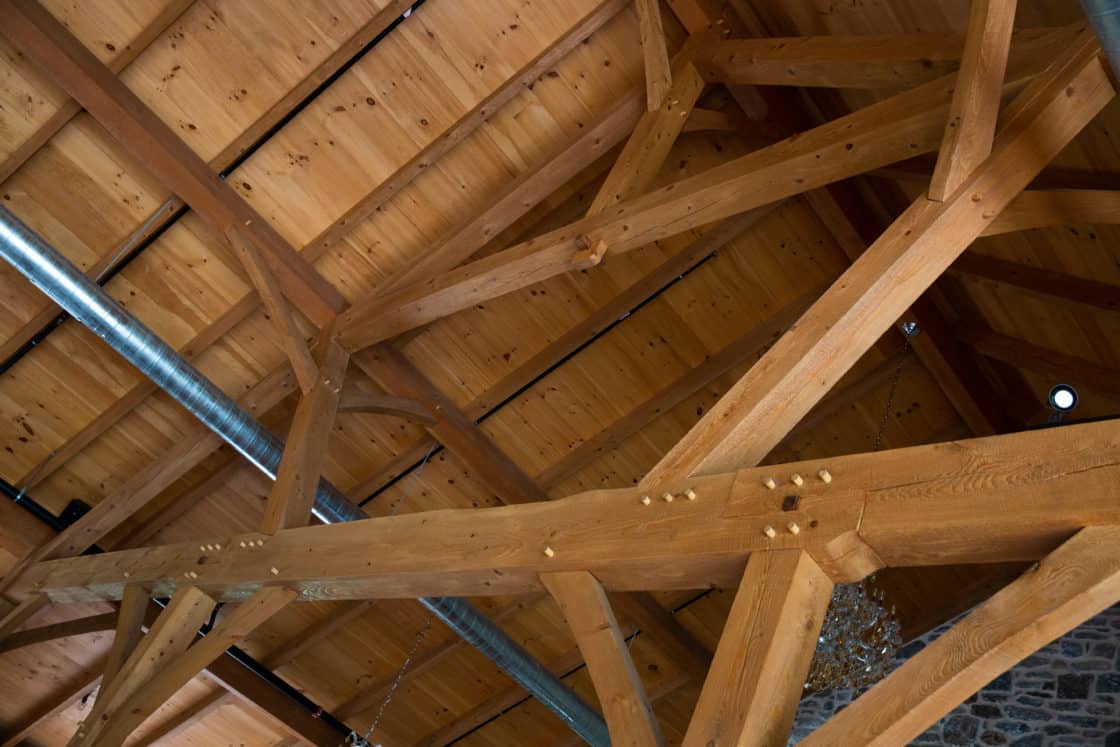 Exposed wooden beams and trusses form the ceiling structure, with visible bolts and a metal air duct running along one side. The light wood and rustic, unfinished look evoke the charm of a luxury horse barn.