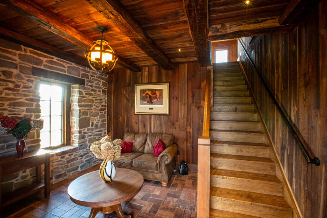 wooden stairway sitting next to small waiting area with loveseat and wooden table