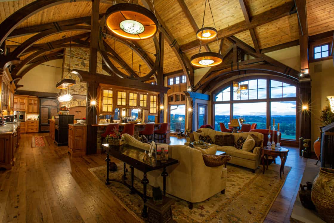 Spacious, rustic living room with vaulted wooden ceilings, exposed beams reminiscent of a luxury horse barn, large windows showing an outdoor view, cozy seating areas, elegant light fixtures, and a warm, inviting atmosphere.