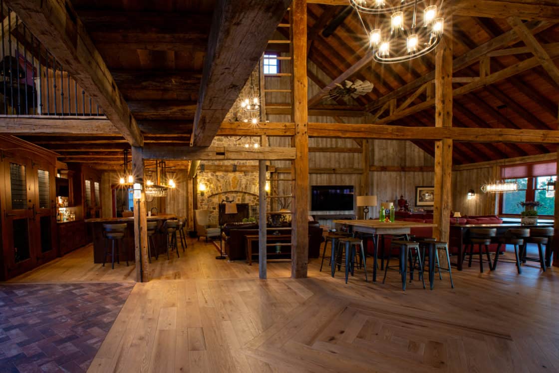 Spacious rustic interior with exposed wooden beams, high ceilings, wooden floors, chandeliers, and cozy seating—this luxury horse barn blends vintage charm with modern comfort for a truly unique gathering space.