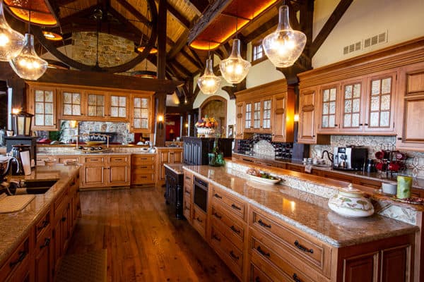 Spacious kitchen with wooden cabinets, stone countertops, exposed beams, and modern appliances. Decorative accents and a large arched window create a warm, rustic atmosphere perfect for a luxury home or elegant bank barn conversion.