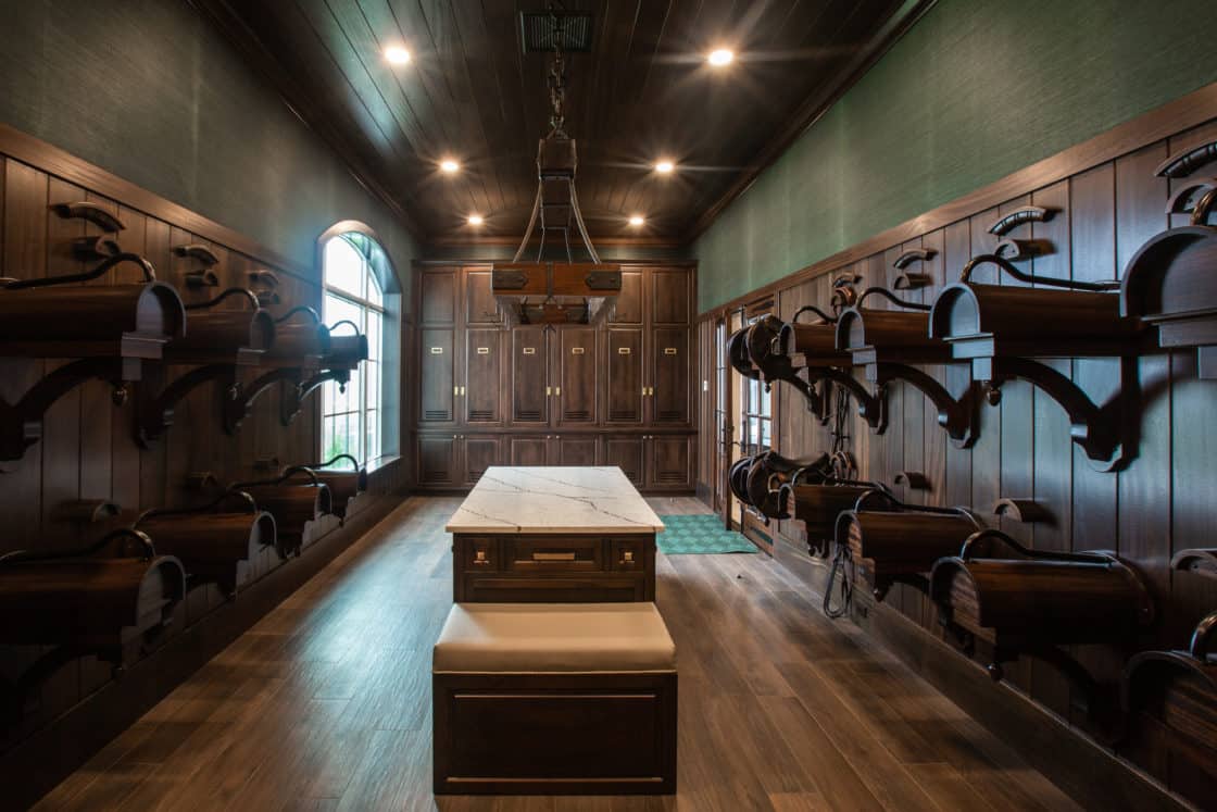 A luxurious golf locker room with dark wood lockers, wall-mounted shelves for golf bags, a marble-topped bench, and soft ceiling lighting evokes the refined elegance of a luxury horse barn reimagined for the avid golfer.