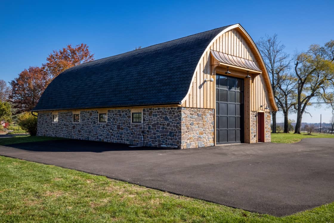 custom built garage with stone siding and asphalt shingles surrounded by pavement