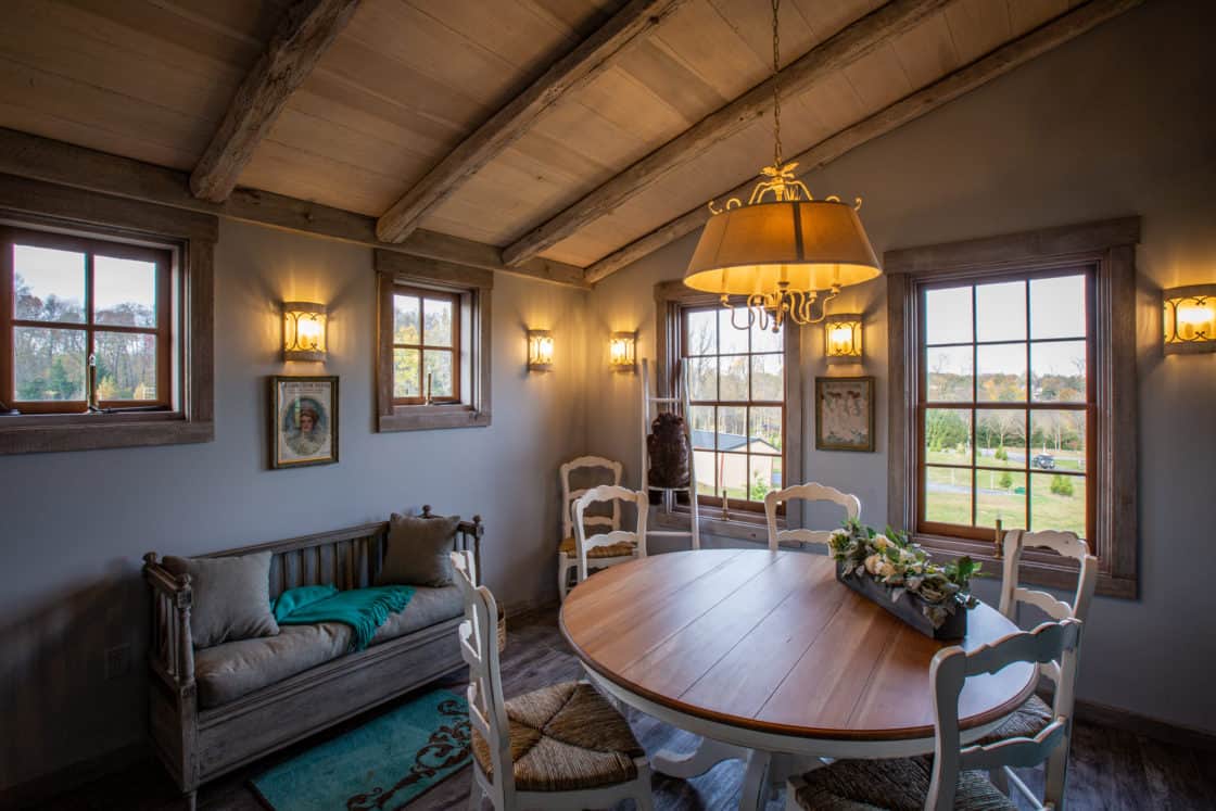 indoor table and chairs sitting next to window overlooking green grass in newly restored barn