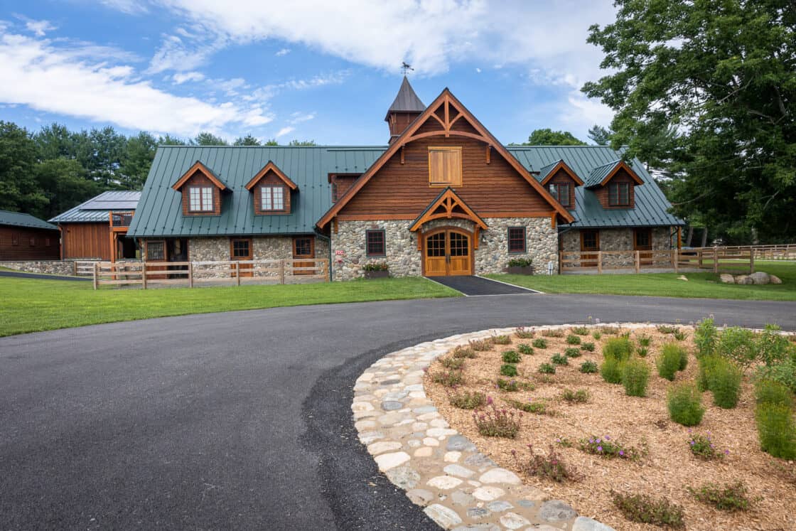 custom built equine facility sitting beneath a day time sky and behind a paved driveway