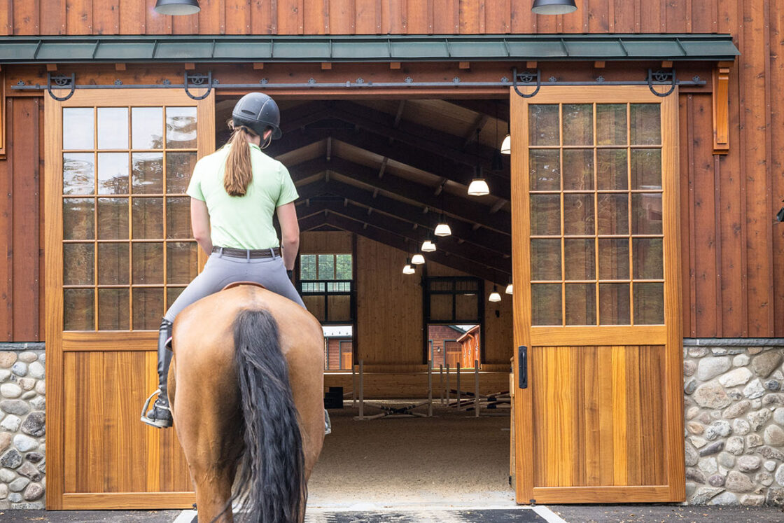 horse and rider heading toward the entrance of a horse barn with windows visible above them
