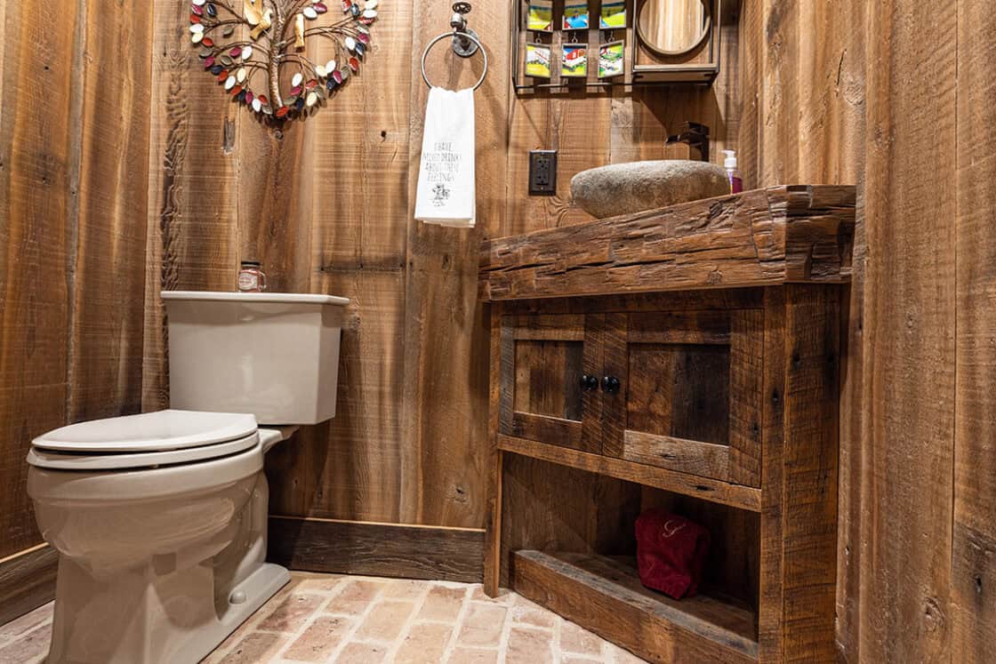 Custom built bathroom with a hand hewn beam sink which sites next to a tan colored toilet which sits beneath a decorate piece above