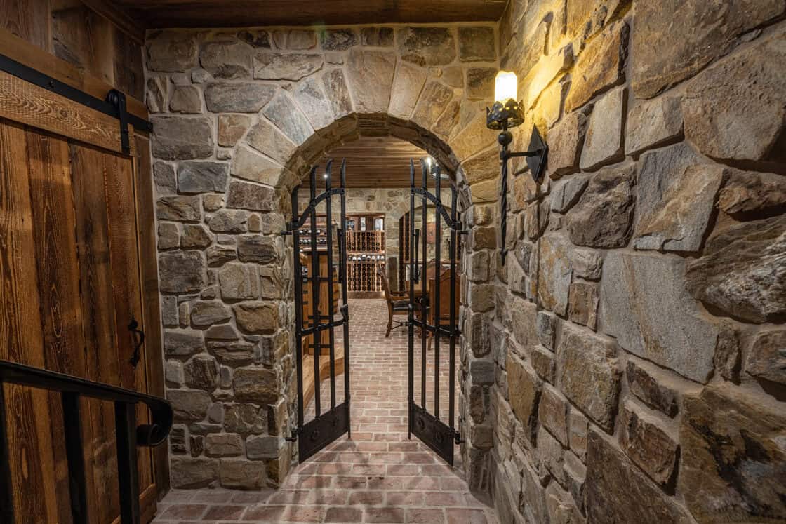 Arched entranceway to wine cellar with open iron gates sitting above a brick floor with the view of a bottle rack in the rear of the room