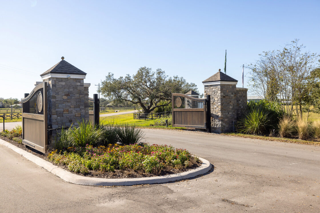 custom built entrance to an equine facility with opened wooden gates sitting beneath a blue sky