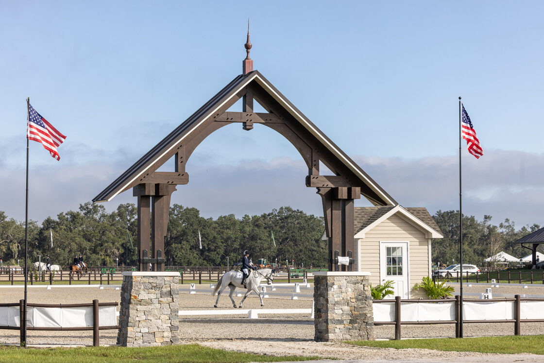 horse and rider visible through the arch walkway with two american flags on each side which sit beneath a clear sky