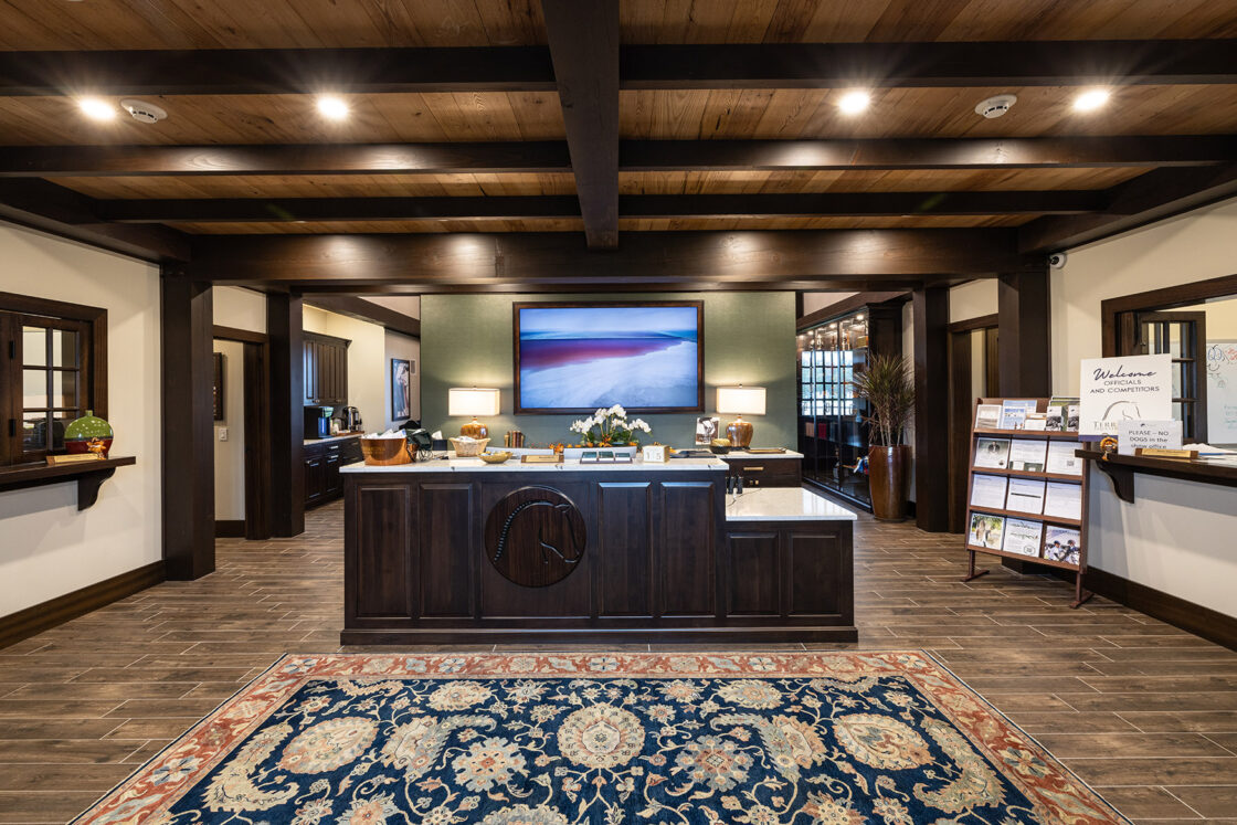 front desk with a horse head carved on it which sits in front of a painting of the shoreline which sits beneath wooden ceiling beams