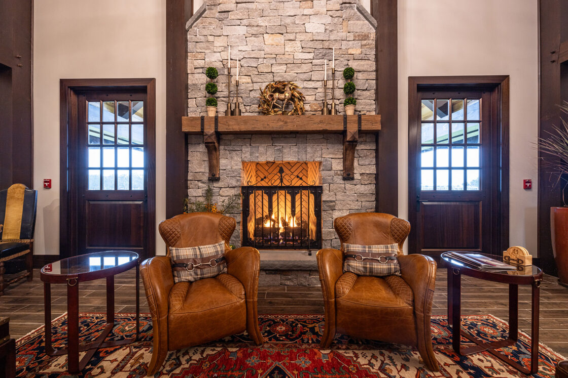 custom built living room with stone fireplace sitting behind two leather chairs that sit atop a large rug with two wooden doors visible behind it
