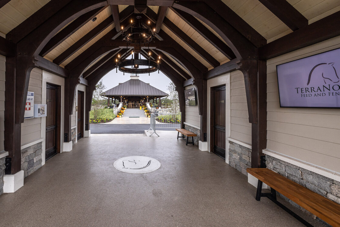 walkway which sits beneath dark wood beams and two hanging light fixtures with a pavilion visible in the back