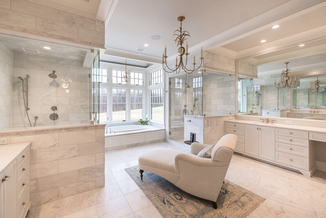 large open space luxury home bathroom with marble colored flooring and siding with a shower and sink to the left, a chair in the middle, and a shower to the right