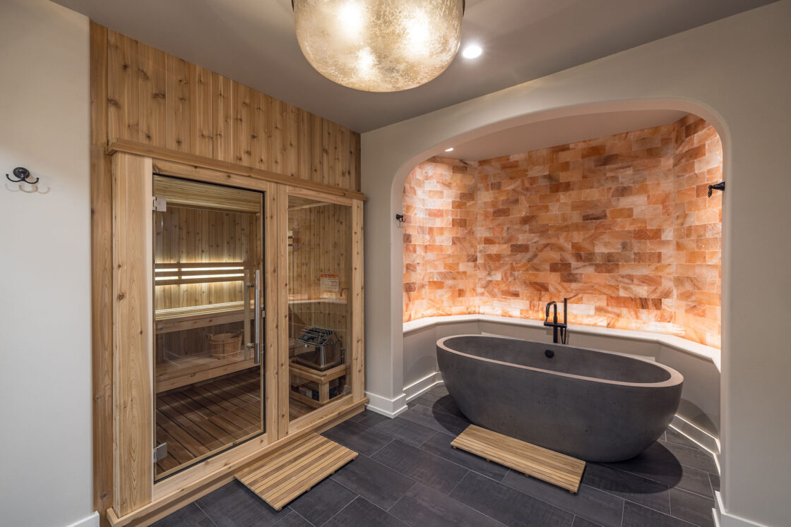 bathtub inside a luxury home with Himalayan salt color siding sitting above it with a sauna sitting to its left which sits beneath a spherical hanging light fixture which illuminates the room