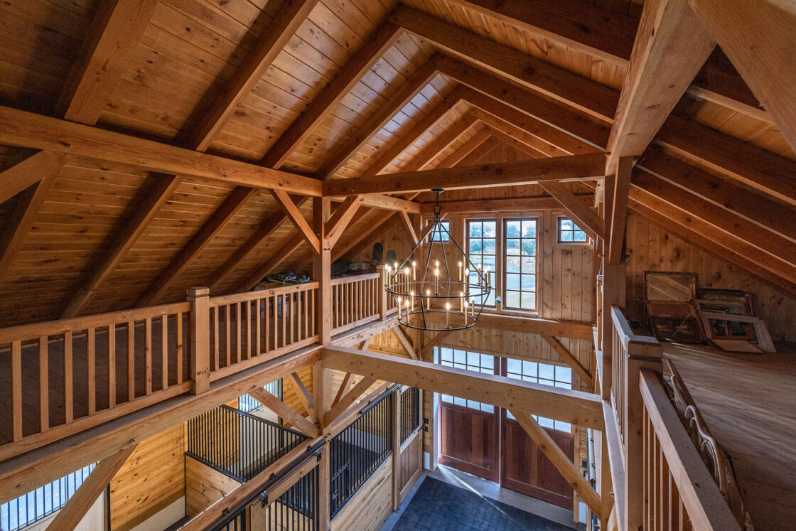 horse barn interior with heavy timber wooden beams and a hanging light fixture in the middle