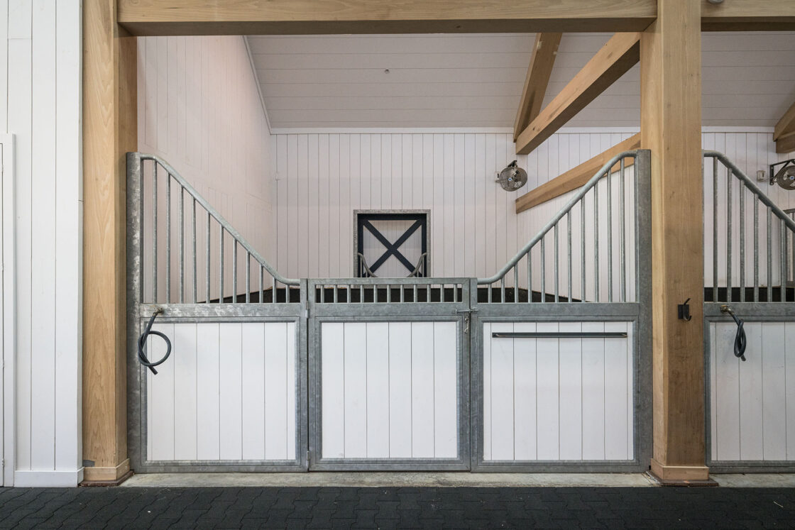 custom built white horse stall with two timber beams on each side sitting behind a paver floor