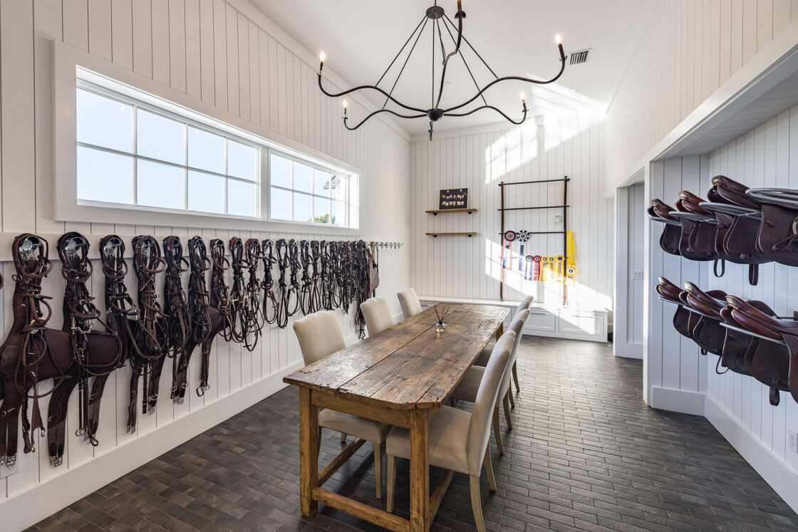 tack room with white walls and hanging metal light fixture resting directly above a wooden table