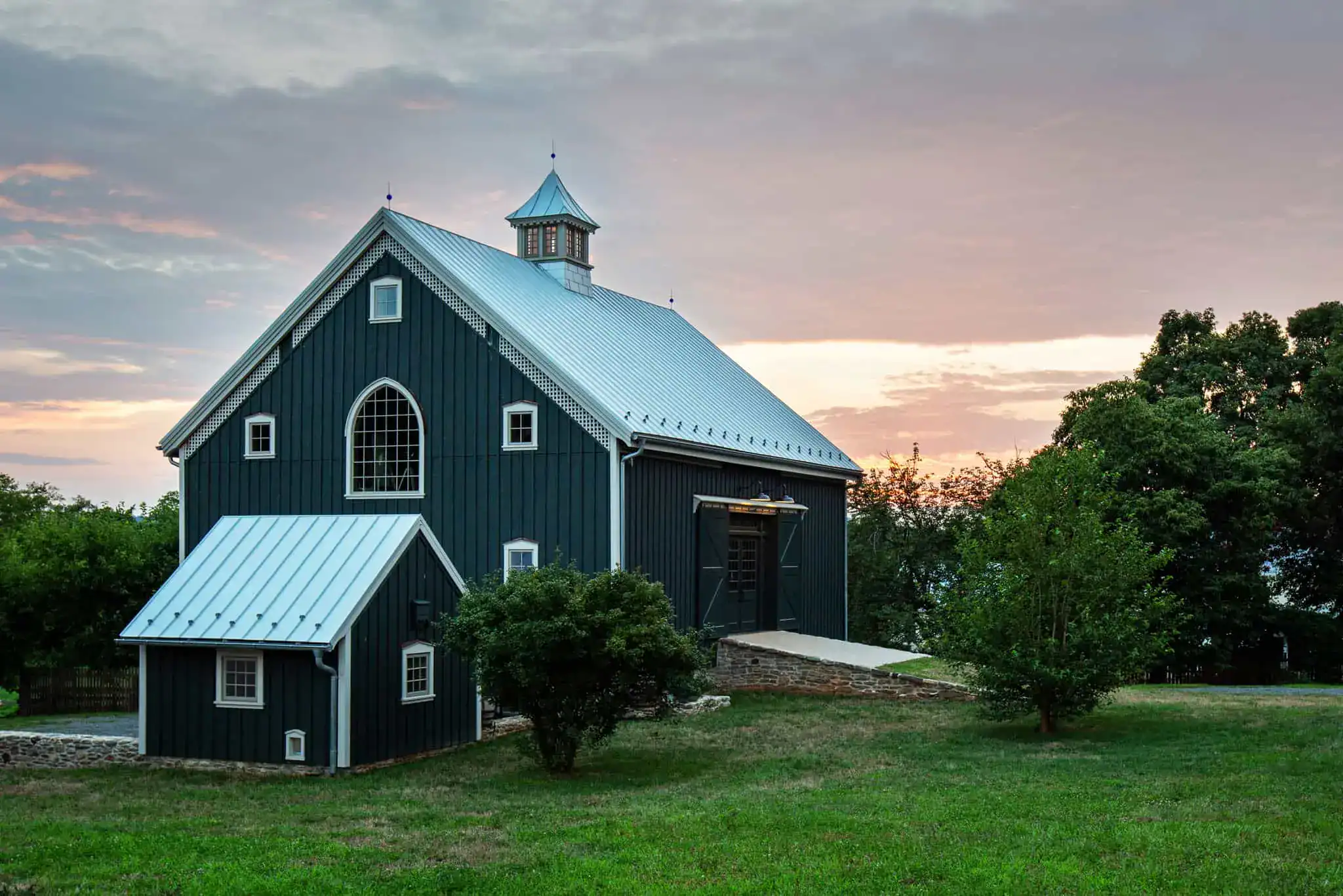 custom barn bd builders custom built barn with a single cupola and metal roof sitting beneath an evening sky with two bushes out front