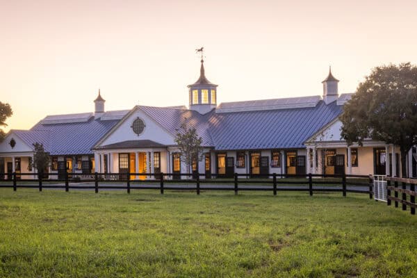 equestrian facility with solar panels on its roof sitting behind a traditional wooden fence and beneath a morning sky