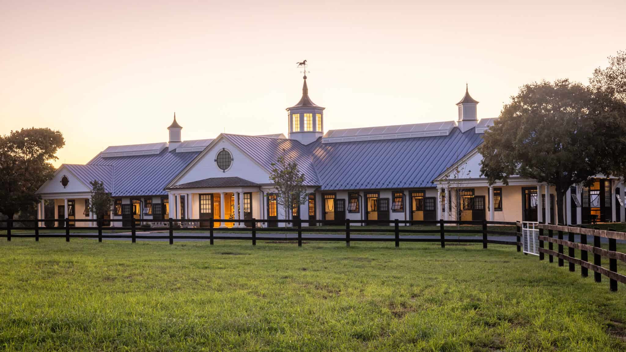 Top Mistakes to Avoid When Designing a Horse Barn equestrian facility with solar panels on its roof sitting behind a traditional wooden fence and beneath a morning sky