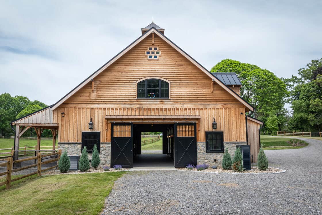custom horse barn with wood siding sitting beneath a cloudy sky