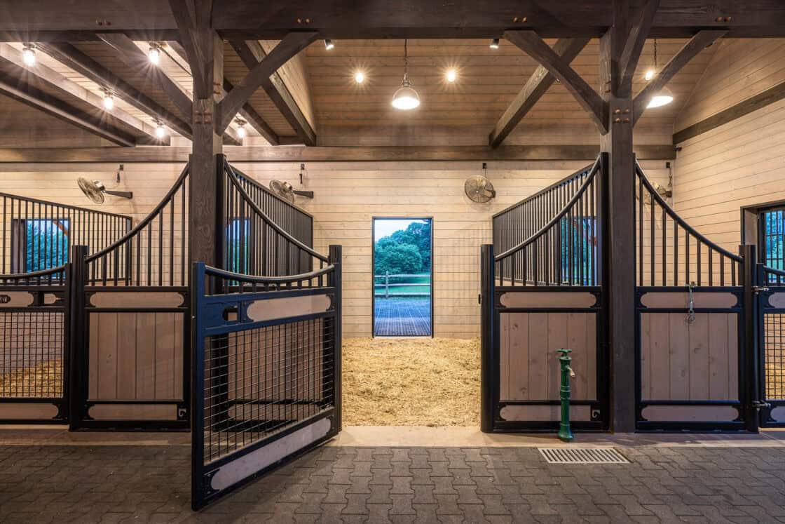 custom horse stall with open gate sitting beneath illuminated light fixtures