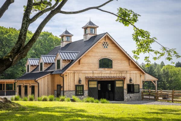 custom built horse barn with a tree branch visible over top with cloudy sky behind it