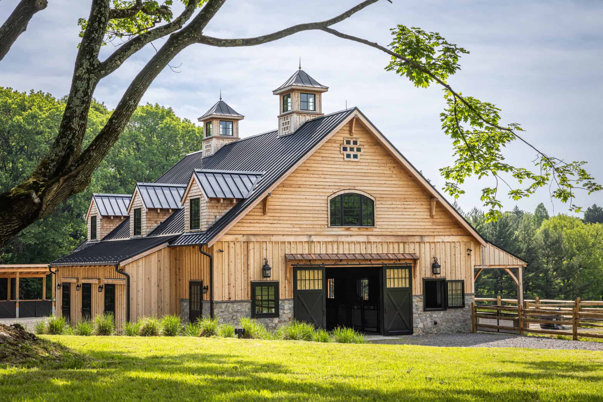 Simply Elegant: Why Less Is More in Equestrian Barn Design custom built horse barn with a tree branch visible over top with cloudy sky behind it