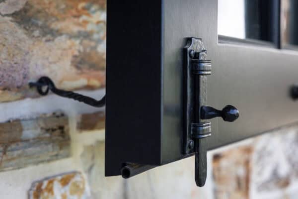 Close-up of a black metal window latch securing an open window to a stone wall, showcasing detailed hardware and textured stone—a refined touch suited for a luxury horse barn or elegant luxury home.