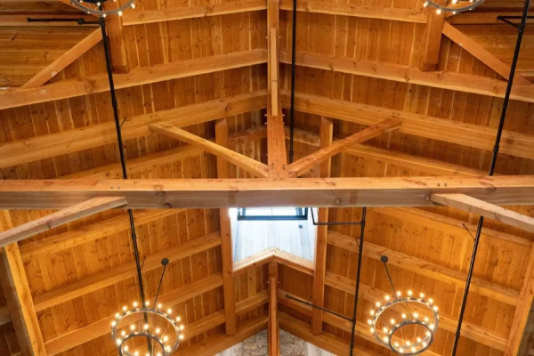 Wooden vaulted ceiling with exposed beams, three circular chandeliers with small lights, and a stone accent wall below a window letting in natural light create the perfect setting for a luxury party barn.