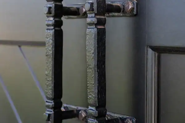 Close-up of two ornate, black metal door handles mounted on a dark wooden door with decorative paneling—perfect for adding a rustic touch to a luxury horse barn. The textured handles are attached with visible bolts for added charm.