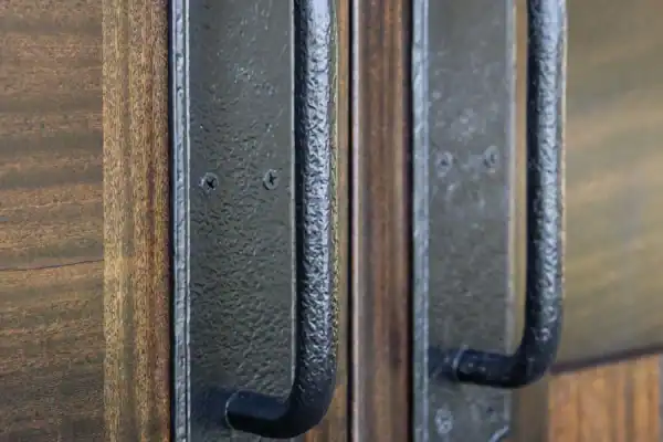 Close-up of two black metal door handles on a pair of dark wooden doors, with a vertical seam where the doors meet—perfect for a luxury horse barn or elegant bank barn entrance.