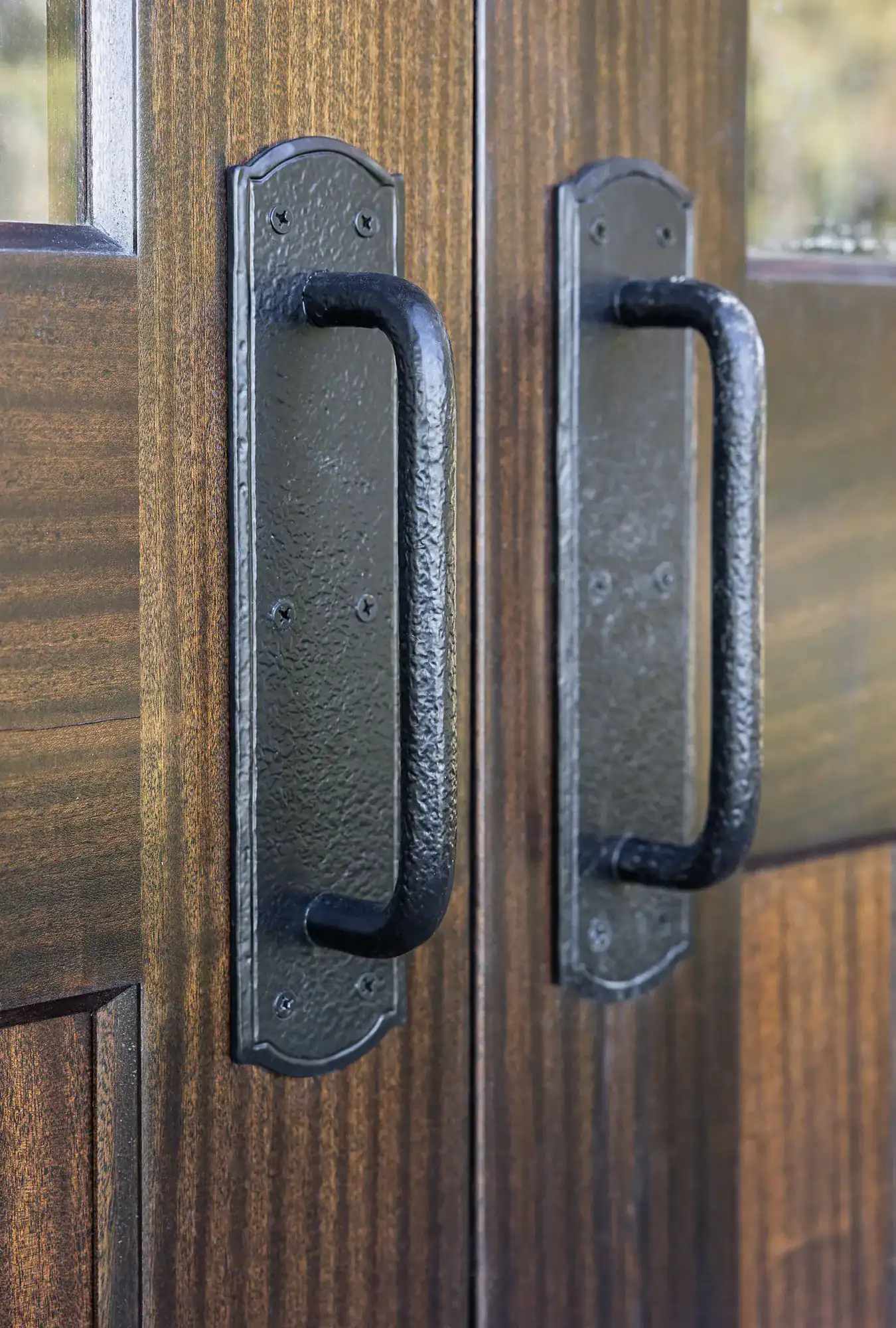 Close-up of two black metal door handles on a pair of dark wooden doors, with a vertical seam where the doors meet—perfect for a luxury horse barn or elegant bank barn entrance.