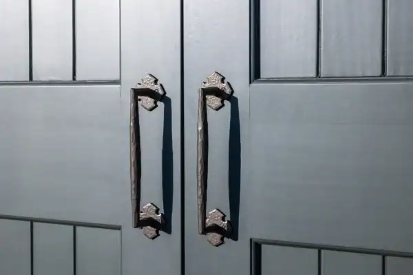 Close-up of two black metal handles on double gray paneled doors, showcasing a textured finish and detailed grooves—perfect for adding a touch of luxury home style to any party barn or bank barn entrance.