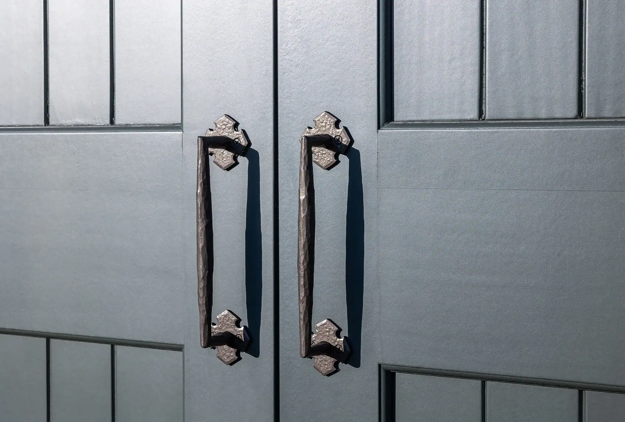 Close-up of two black metal handles on double gray paneled doors, showcasing a textured finish and detailed grooves—perfect for adding a touch of luxury home style to any party barn or bank barn entrance.