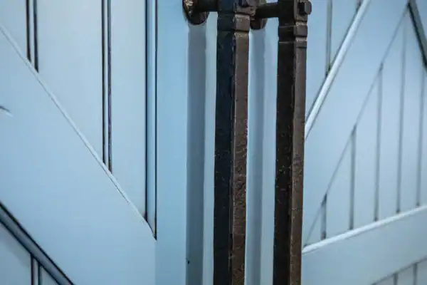 Close-up of two large, black metal door handles mounted vertically on a light blue, wooden barn-style door with diagonal and vertical panels—an elegant touch often seen in luxury home or bank barn designs.
