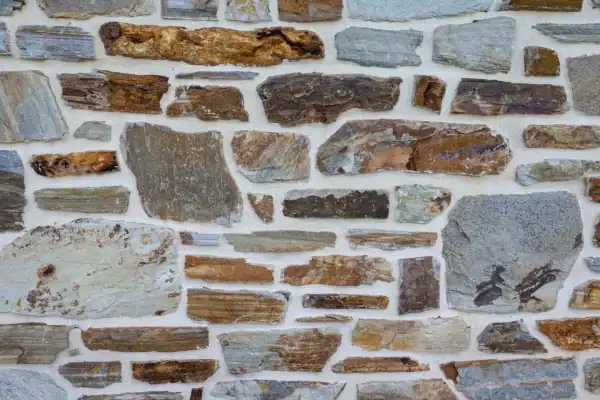 A close-up of a stone wall, reminiscent of those found in a bank barn, with irregularly shaped stones in shades of brown, gray, and tan held together by white mortar.