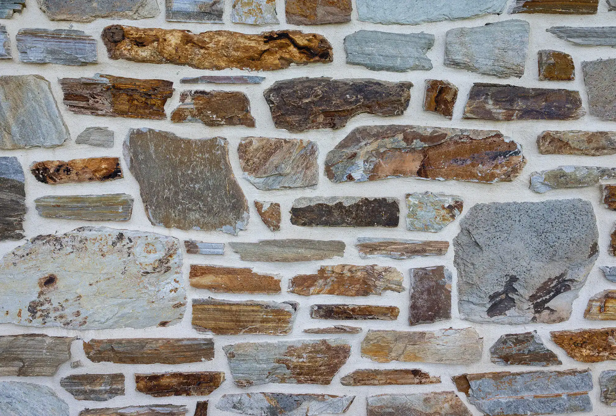 A close-up of a stone wall, reminiscent of those found in a bank barn, with irregularly shaped stones in shades of brown, gray, and tan held together by white mortar.