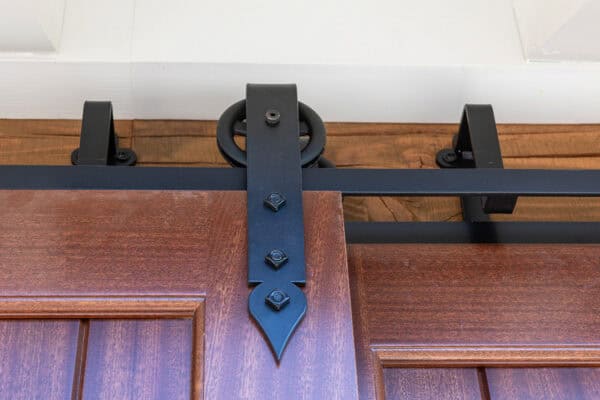 Close-up view of a sliding barn door system in a luxury horse barn, featuring the metal track, black hardware, and upper edge of a wooden door with decorative detailing.